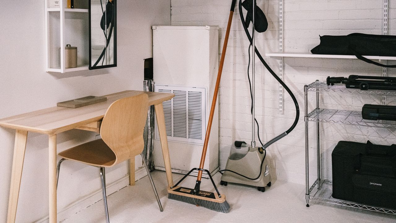A neat home office setup with a wooden desk, chair, broom, and cleaning supplies.